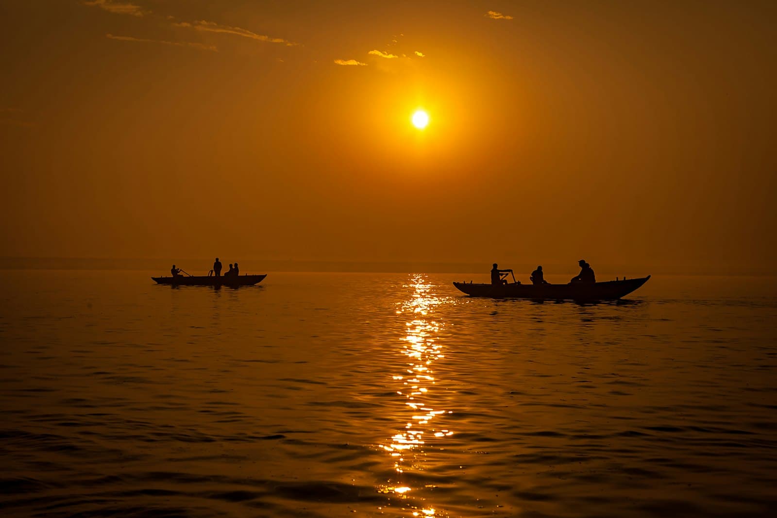 Silhouetted rowing boats on the Ganges at Varanasi under a golden sunrise
